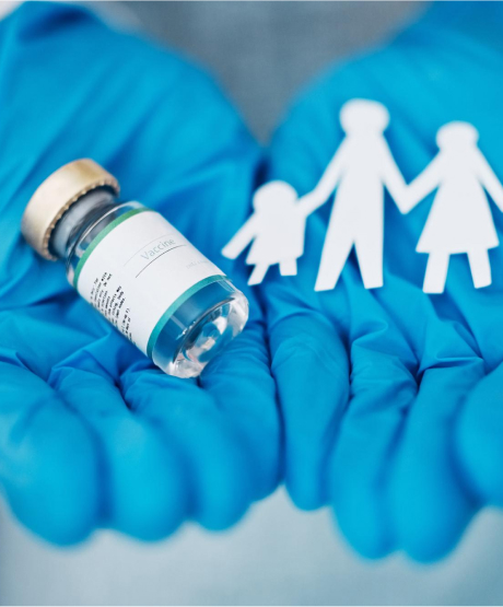 A pair of blue-gloved hands holding a vaccine vial on the left and paper cutouts of a family on the right, symbolizing vaccination and family health.