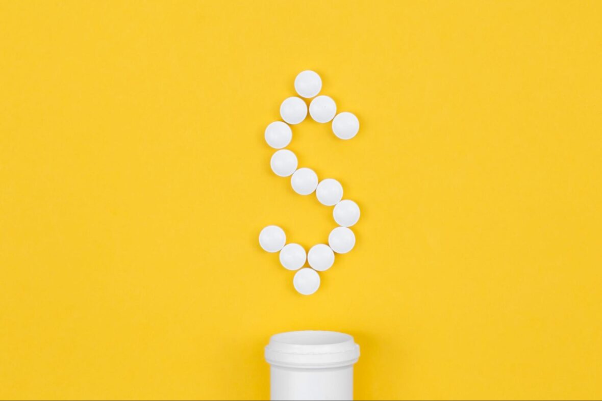 White pills arranged in the shape of a dollar sign above the opening of a white pill bottle, set against a bright yellow background.